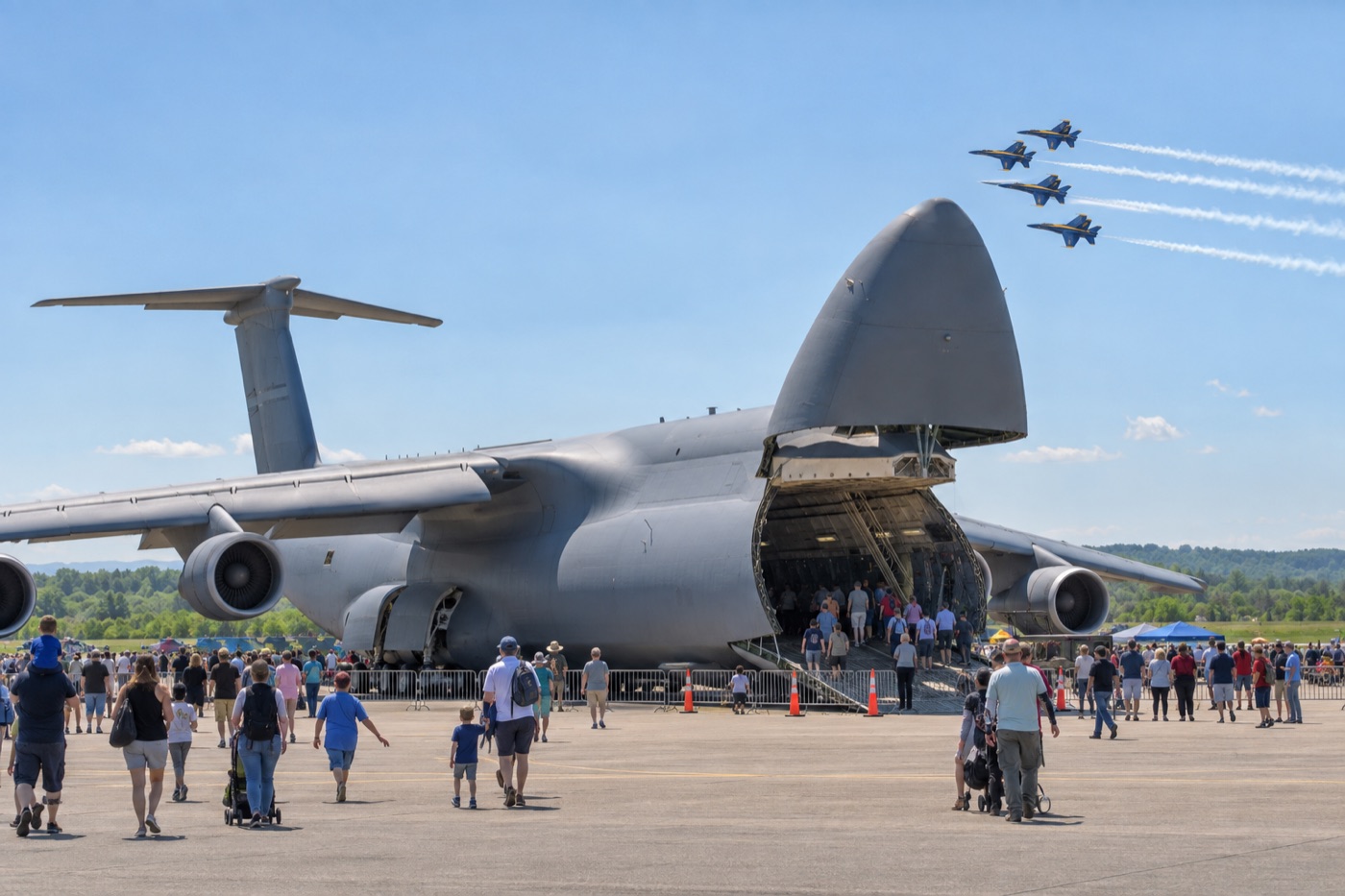 Families approaching a huge military transport aircraft at an air show while jets fly overhead