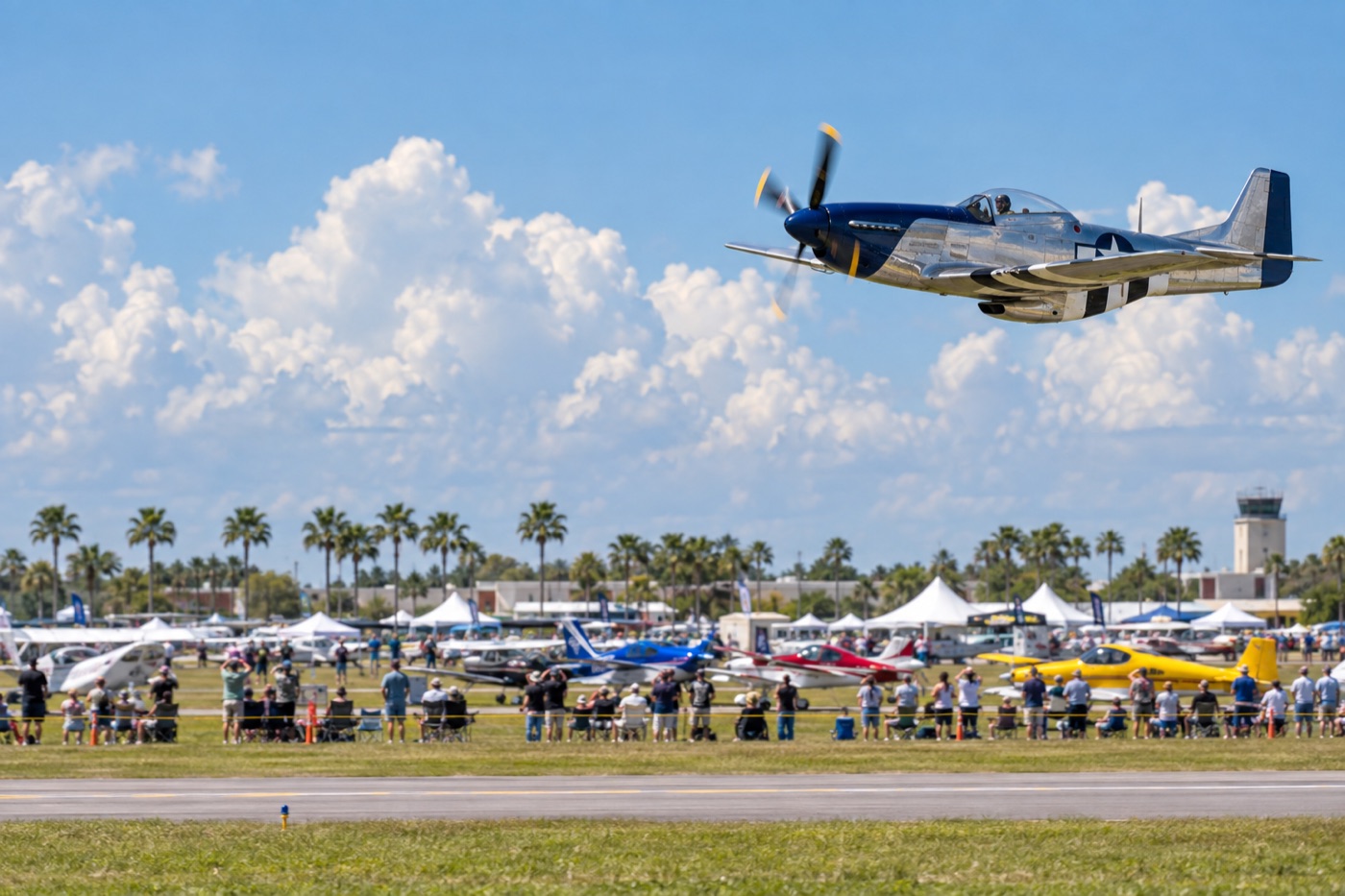 A polished propeller warbird flying past a busy Florida air show