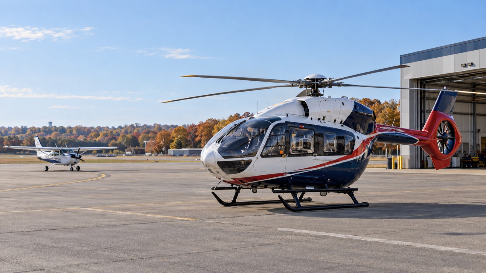 A medical helicopter parked outside a hangar as a small high-wing airplane arrives on the ramp